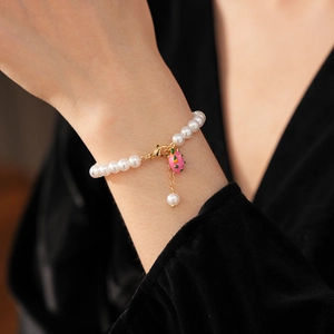 Detail of pearl bracelet featuring a pink fruit pendant worn on a female wrist
