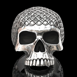 Detailed close-up of a silver skull ring featuring chainmail texture on top and dark shadows