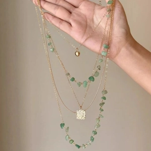 Detail of layered gold necklaces featuring green crystal beads and heart-shaped charms