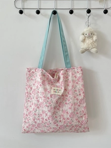 Pink floral quilted tote bag with blue straps and cute bear charm shown on white wall