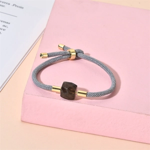 Détail du bracelet tissé gris avec pierre brune carrée sur un support rose chic