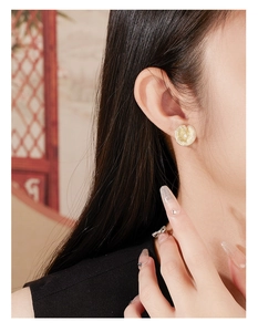 Detail of gold petal earrings with brushed texture and zircon on a model's ear