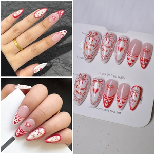 Detail of red heart almond press-on nails with bow accents and pearl decorations