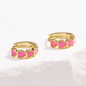 Close-up of gold hoop earrings featuring a row of small pink enamel hearts on stone surface