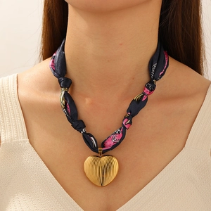 Detail of a vintage gold heart pendant with vertical texture and floral silk ribbon chain