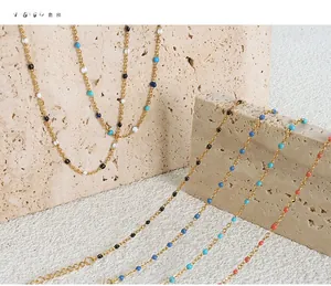 Detailansicht der bunten Emaille-Perlenketten aus Gold auf einem natürlichen Travertinstein