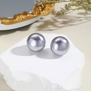 Detail view of large mauve faux pearl stud earrings on a minimalist stone surface