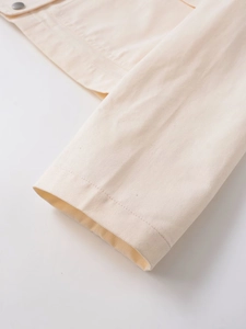 Détail de la manche d'une veste en coton beige clair avec bouton métallique argenté