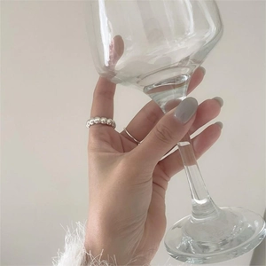 Minimalist 925 sterling silver beaded ring shown on a finger holding a glass