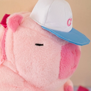 Close-up of pink capybara plush backpack featuring a blue baseball cap with C embroidery