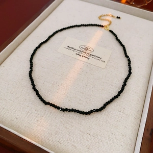 Detail of a minimalist black beaded necklace with a gold clasp on a beige tray