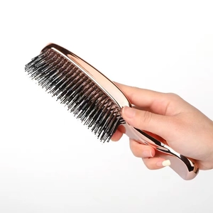 Detail shot of a handheld rose gold scalp massage comb with black bristles on white backdrop