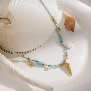 Détail macro du collier tressé avec pendentifs hippocampe et coquillage dorés sur assiette