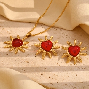 Detail of 18K gold-plated necklace and heart earrings on beige stone backdrop