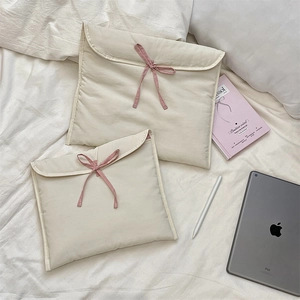 Dettaglio custodia trapuntata crema per laptop con fiocco rosa su letto bianco
