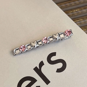 Detail of silver metal hair clip featuring pink rhinestones and heart relief design