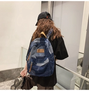 Detail view of vintage denim patchwork backpack with brown leather patch and white stitching