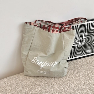 Detail of sage green nylon tote bag featuring Bonjour magic print and plaid lining