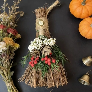 Detail of festive decorative broom with dried flowers, pine cones and a golden sun charm