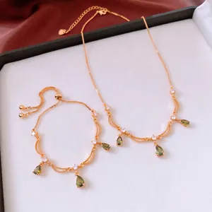 18k vergoldetes Schmuckset mit grünen tropfenförmigen Anhängern auf rotem Seidenhintergrund