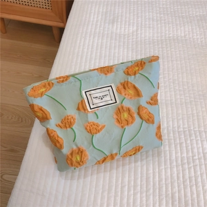 Detail of light blue cosmetic bag with orange poppy embroidery on a white bed