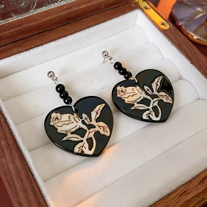 Close-up of black heart earrings with gold rose pattern on white velvet lining