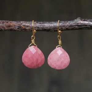 Macro detail of pink teardrop emperor stone earrings with gold wire wrap on a wooden branch