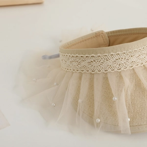 Detail of cream straw sun visor featuring elegant lace trim and delicate pearl mesh trim