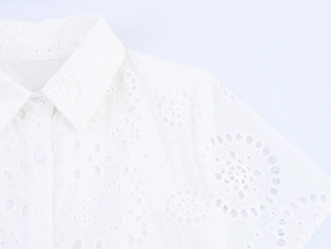 Detailed close-up of a white shirt collar featuring intricate hollow floral embroidery