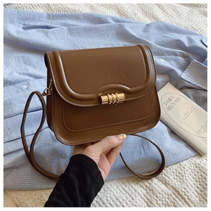 Sacoche vintage en cuir marron avec fermoir doré tenue devant une chemise à rayures bleues