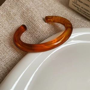 Detailed view of an amber resin open bangle on a ceramic dish with textured fabric background