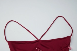 Detail of red backless dress showing thin straps and pink droplet decoration on fabric