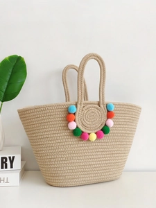 Handmade woven straw tote bag in beige with colorful pompom charms and minimalist aesthetic