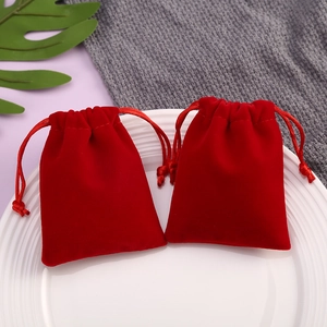 Close-up of two red velvet drawstring jewelry pouches on a white decorative plate