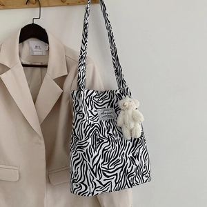 Detailed shot of a zebra print canvas tote bag with an Augur label and plush bear charm