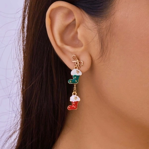 Close-up of Christmas bow stud earrings with green and red stocking pendants on ear