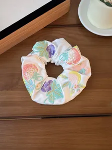 Close-up of white satin scrunchie featuring embroidered strawberry and grape patterns
