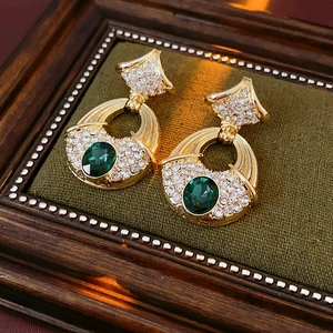 Detail of vintage gold earrings with green gemstones and diamonds in a retro frame