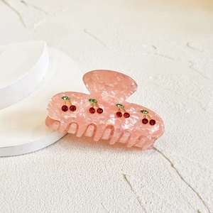 Pink marble hair claw clip with red cherry patterns on a white display stand