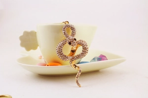 Close-up of a sparkling gold snake keychain with rhinestones on a white ceramic cup
