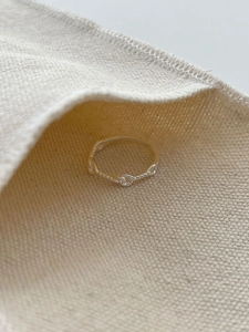 Detailed close-up of 925 sterling silver twisted knot ring on soft beige canvas