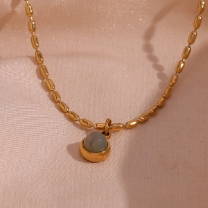 Close-up of 18K gold-plated beaded chain with round grey natural stone pendant on pink silk
