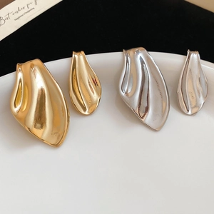 Detail of gold and silver fishtail stud earrings on a white ceramic plate