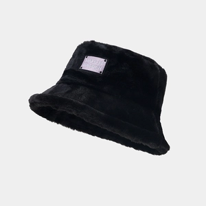 Détail d'un chapeau bob noir en peluche avec patch brodé et texture douce en fausse fourrure