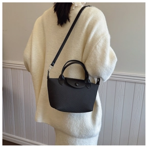 Detail of a black woven dumpling bag with leather flap and detachable shoulder strap