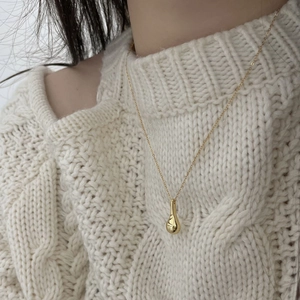 Detailed close-up of a golden waterdrop pendant necklace worn on a white sweater
