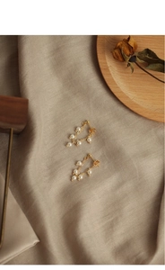 Macro detail of elegant gold earring with natural pearls and tassels on linen fabric