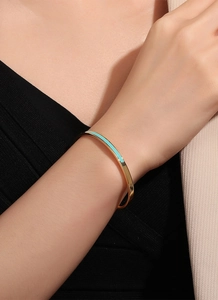 Close-up of golden enamel cuff bracelet with mint green detail on a female wrist