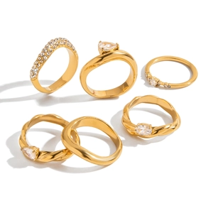Set of six gold plated stainless steel rings with clear zircon stones on white background