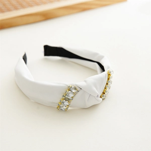 Detail showing white fabric knotted headband with clear rhinestones in gold settings